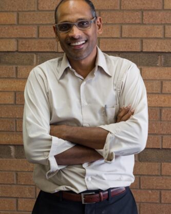 Portrait of Dr. Joseph Pathakamuri standing in front of a brick wall.