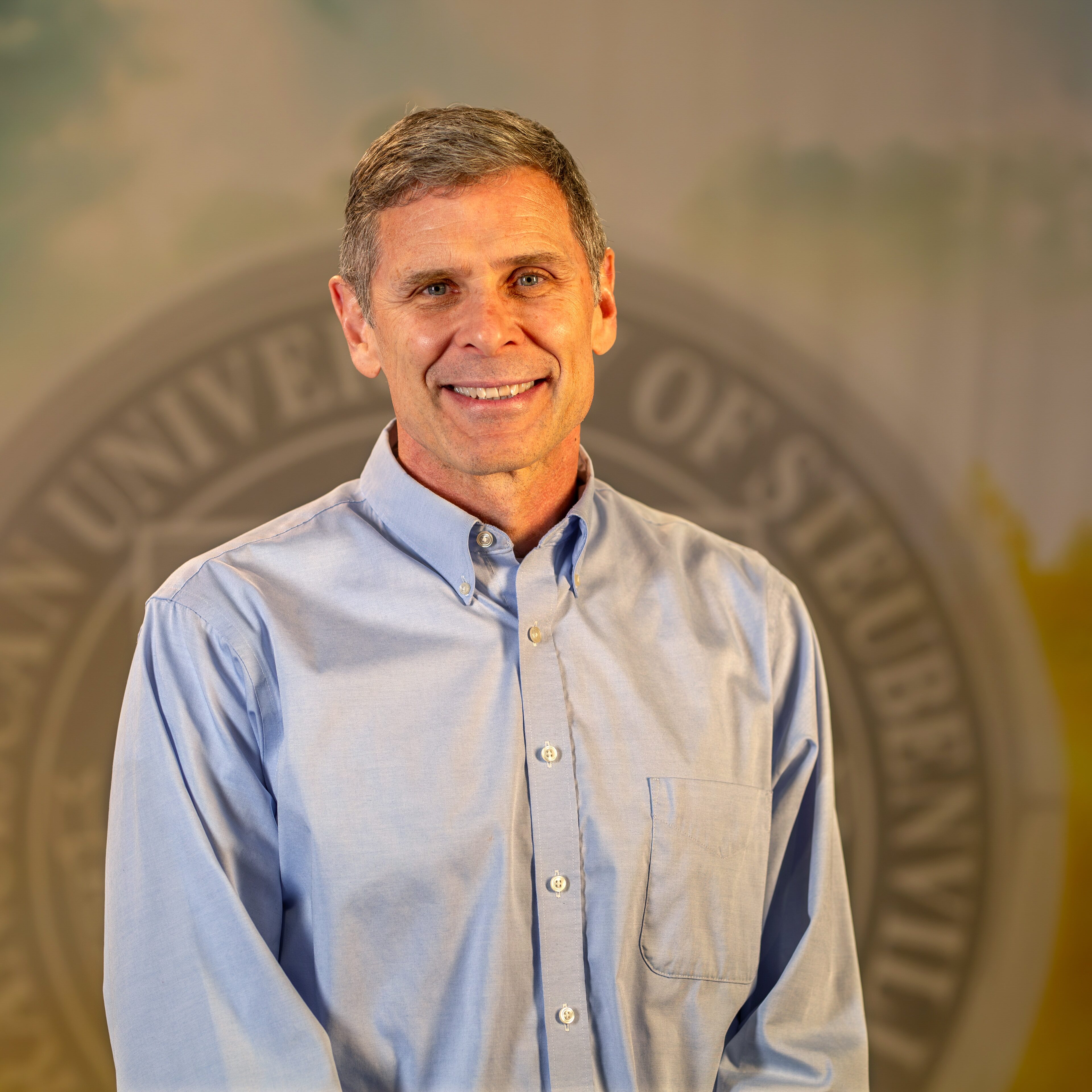To Web – Dr. Jeffrey Rohde FEB2025 –7 Dr. Jeffrey Rohde standing in front of university seal.