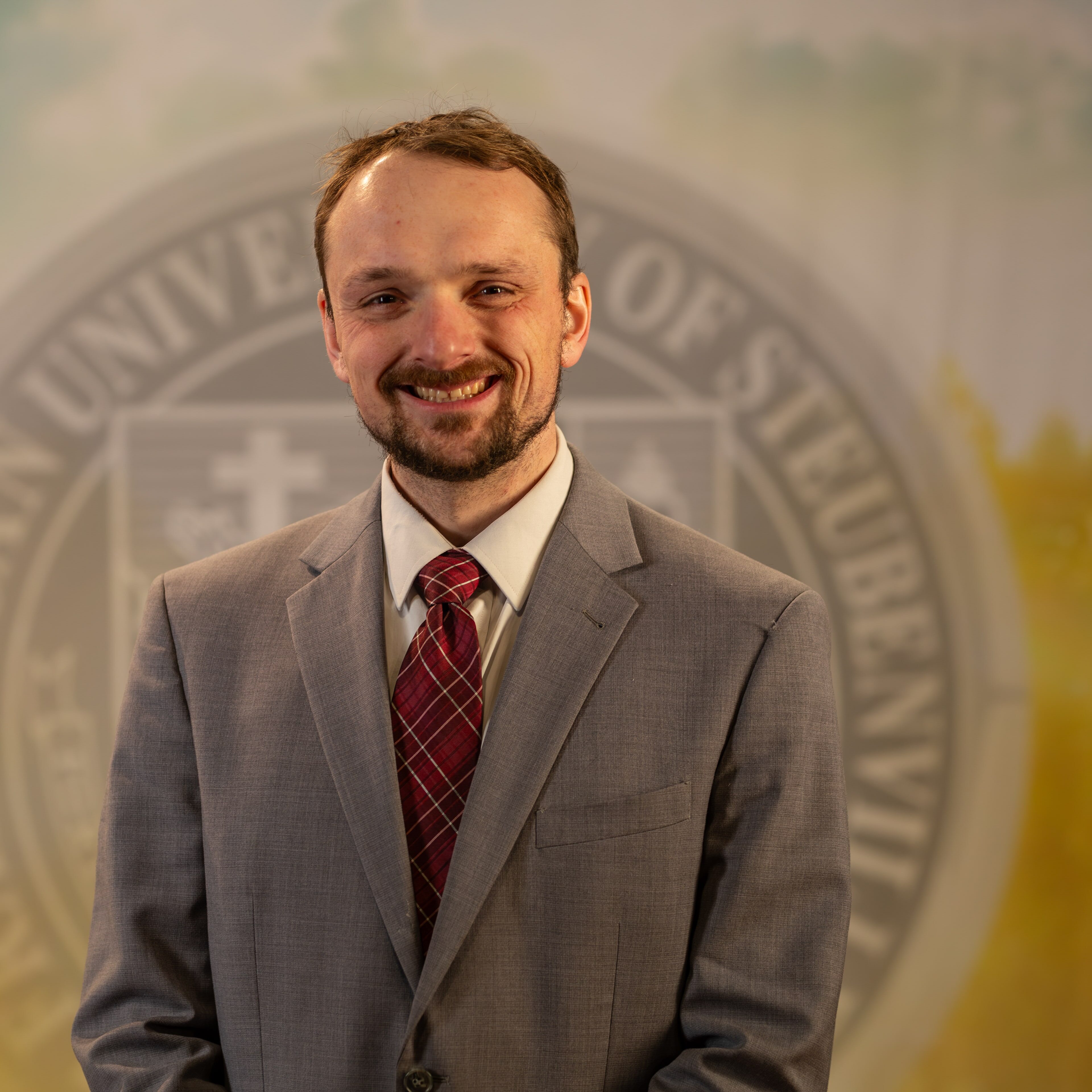 To Web – Dr. Tyler Brown FEB2025 –8 Dr. Tyler Brown standing in front of a university seal.