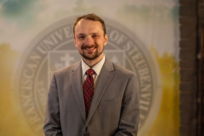 To Web – Dr. Tyler Brown FEB2025 –8 Dr. Tyler Brown standing in front of a university seal.