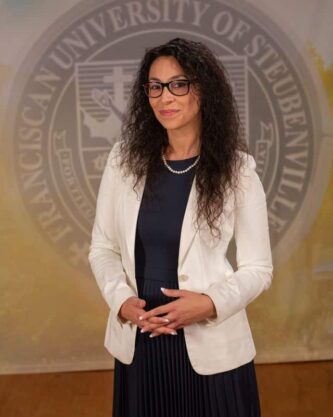 Dr. Fernanda Psihas wearing a dress and white blazer in front of the university seal.