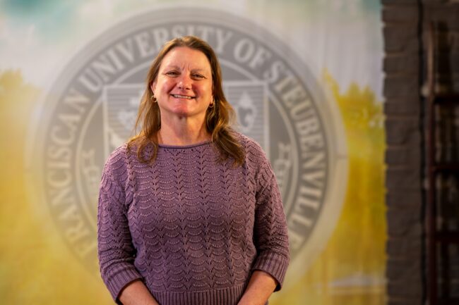 Denise Lombard standing in front of a university seal.