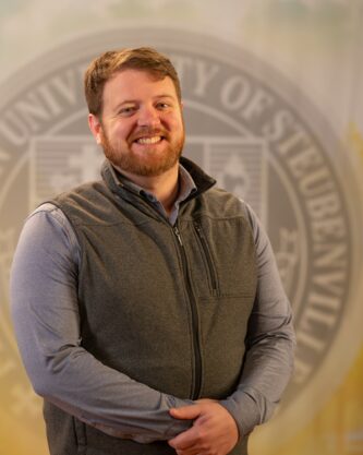 Matthew Cahill standing in front of a college seal.