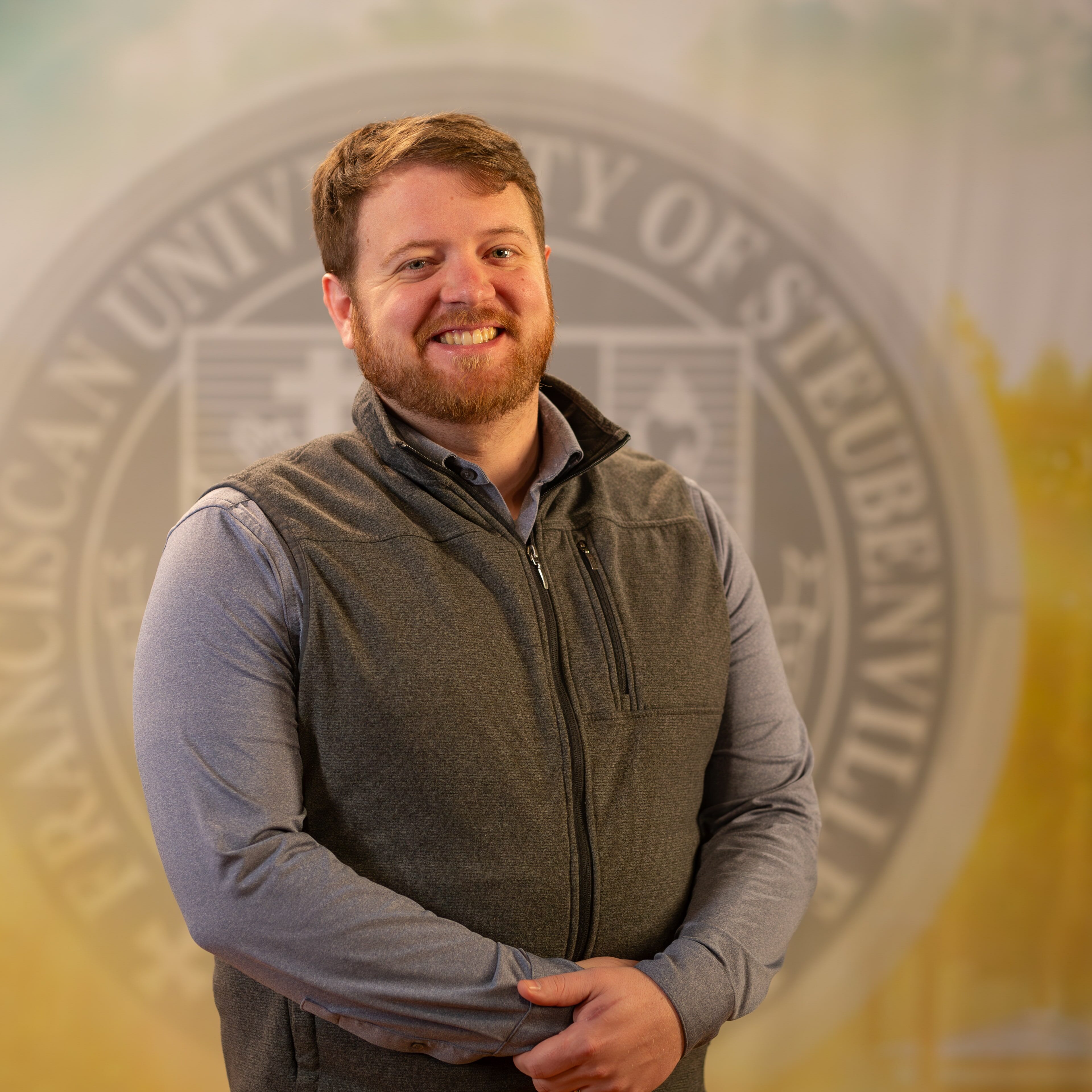To Web – Matthew Cahill FEB2025 –3 Matthew Cahill standing in front of a college seal.
