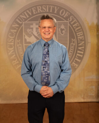 Dr. Tom Web in a professional wear standing in front of a university seal.