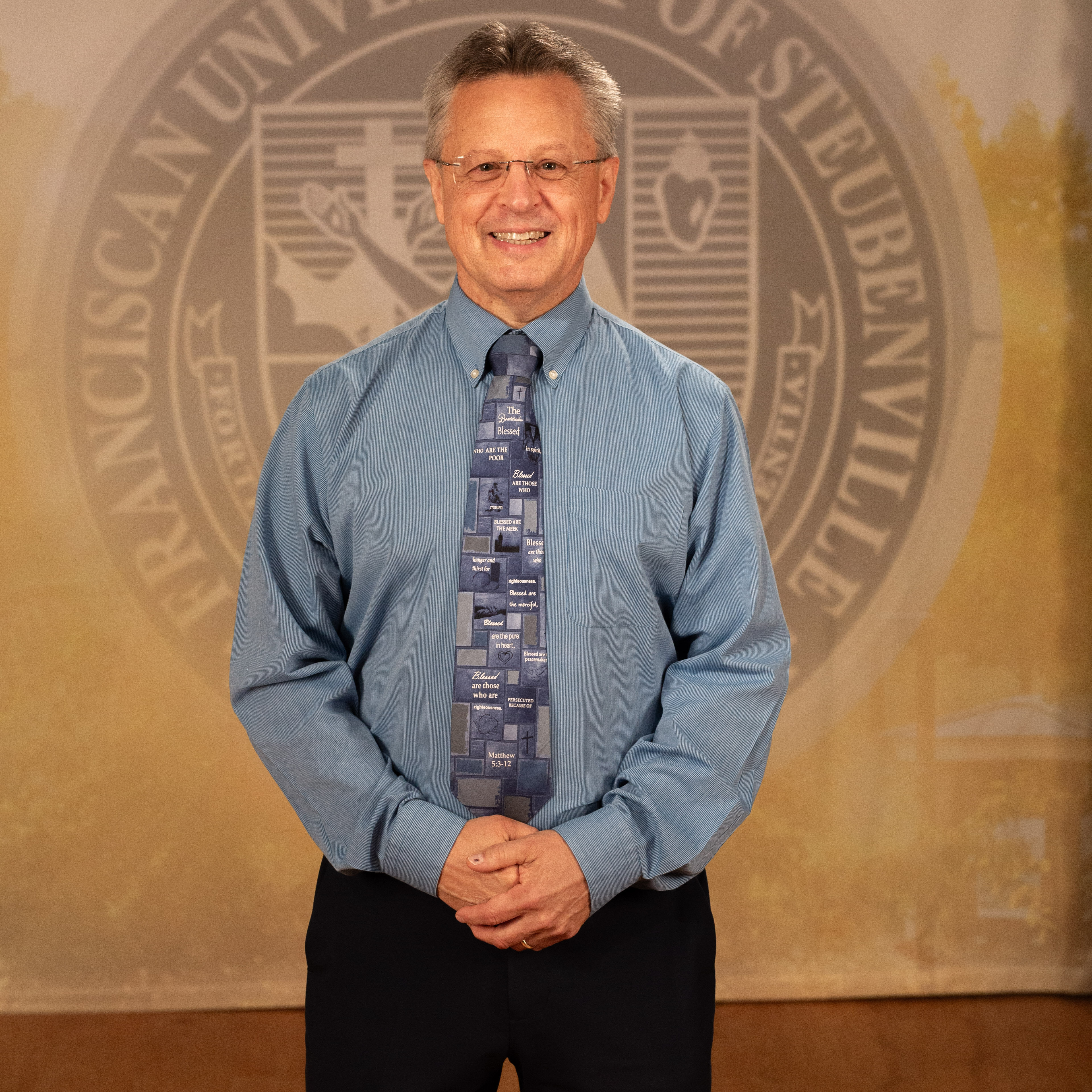 Dr. Tom Webb_FNL__B5A2265 Dr. Tom Web in a professional wear standing in front of a university seal.